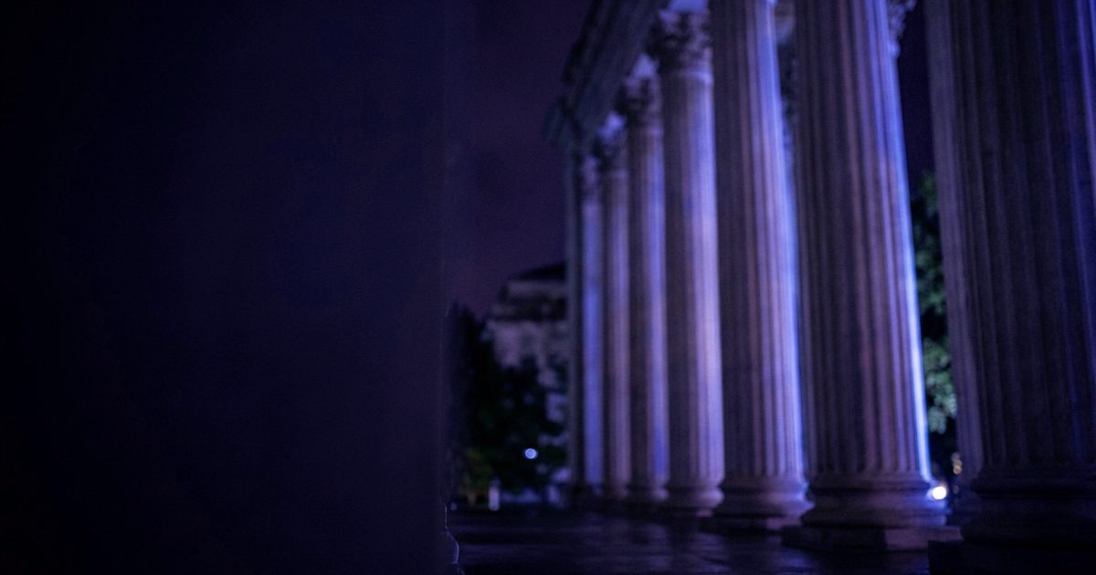 Stone courthouse columns lit in cool blue light at night